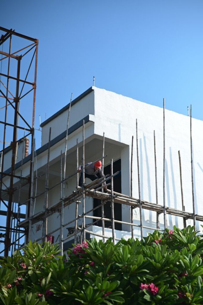 A construction worker stands on scaffolding at a building site under clear blue skies.