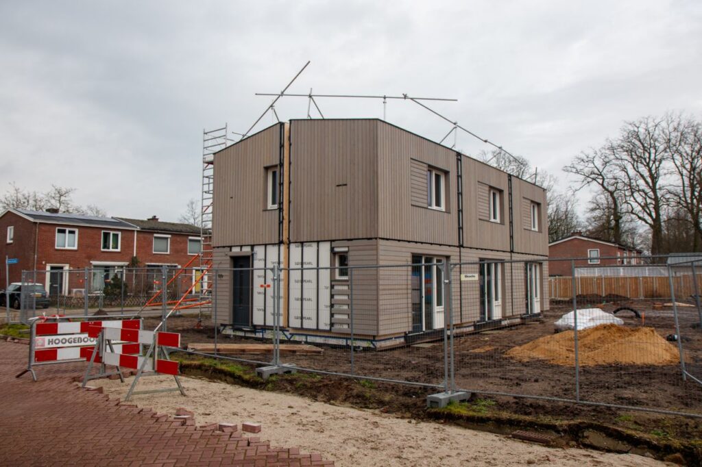 A modern house under construction with scaffolding, fences, and construction signs on a cloudy day.