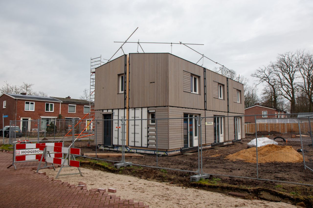 A modern house under construction with scaffolding, fences, and construction signs on a cloudy day.